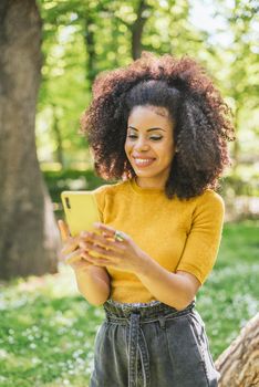 Pretty afro woman typing on mobile, in the forest. Selective focus.