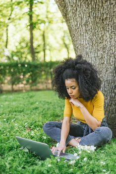 Beautiful afro woman typing on a laptop in a garden. Selective focus.