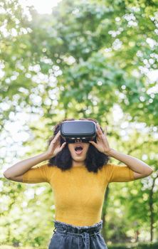 Afro woman wearing a virtual reality glasses in a garden. Selective focus.