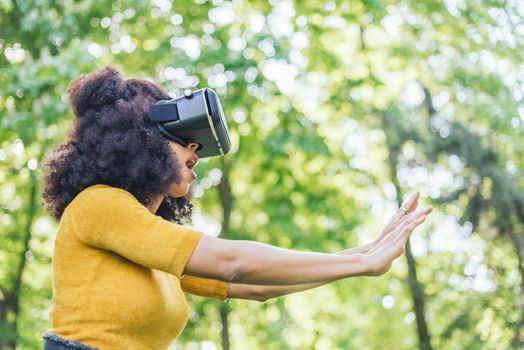 Afro woman wearing a virtual reality glasses in a garden. Selective focus.