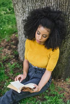 Pretty afro woman reading a book in a garden. Selective focus.