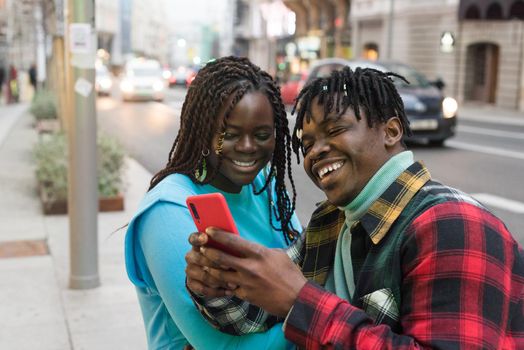 Smiling black couple looking at mobile on the street. Selective focus.