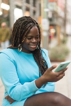 Smiling black girl looking at mobile in the city. Selective focus.