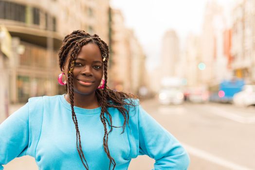 Pretty young black woman in the middle of the city, smiling at camera. Selective focus.