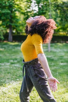 Pretty afro woman breathing fresh air in nature, in a garden. Selective focus.