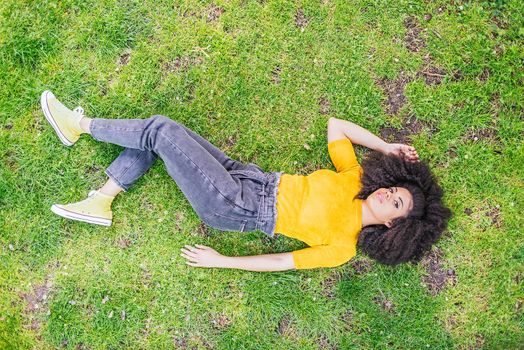 Pretty afro woman lying on her back in a garden. Aerial view. Selective focus.