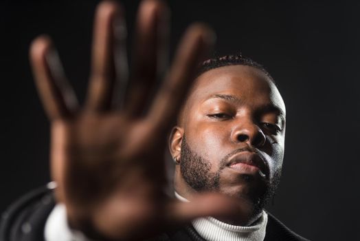 Serious black man telling you to stop with an open hand. Close up. Black background.