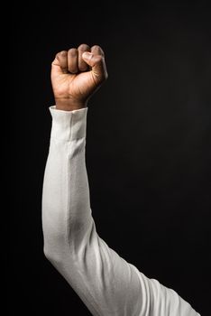 Raised fist of a black man, on a black background, long white sleeves. Close up. Black background.