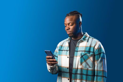 Handsome black man looking at mobile. Mid shot. Blue background.