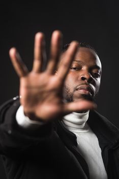 Serious black man telling you to stop with an open hand. Close up. Black background.