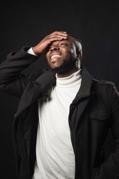 Black man laughing with his hand on his face. Mid shot. Black background.