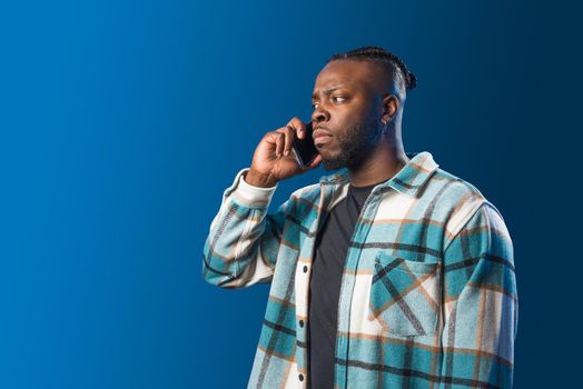 Handsome black man talking on the mobile worried. Mid shot. Blue background.