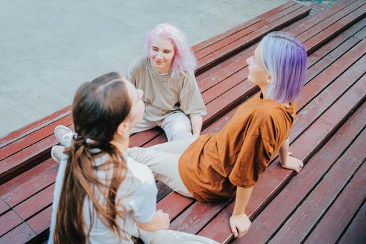 Modern teenage girls with colorful dyed hair sitting on bench in park. Women chatting, gossiping and laughing. Friendship concept. High quality photo
