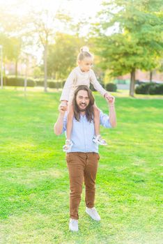 Vertical image of a enthusiastic young father holding her little daughter on his shoulder in park