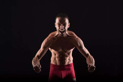 Furious shirtless man showing his muscles. Mid shot. Black background.