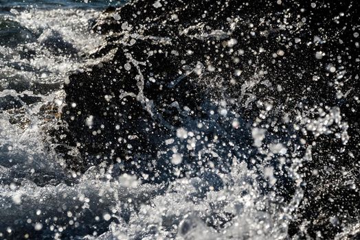 Detail of a wave breaking on the shore against a rock, splashing many drops of water. Fast shutter frozen motion.
