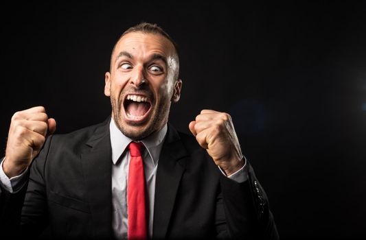 Euphoric man in suit celebrating something. Black background. Close up.