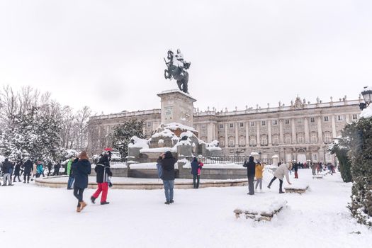 Equestrian statue of King Felipe IV with the Royal Palace of Madrid behind on a winter day after a heavy snowfall.