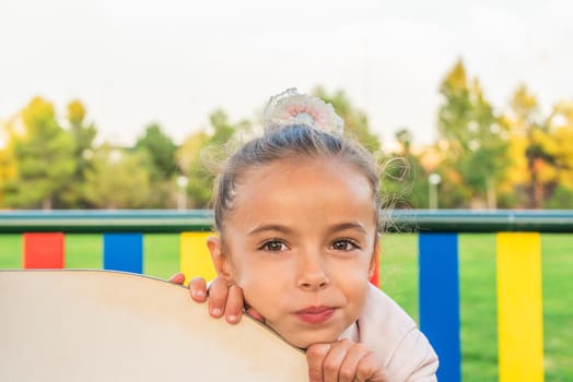 Portrait of a little girl leaning with her hands and chin on a playground set.