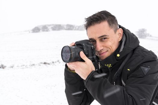 Smiling photographer taking photos in a snowy landscape on a cold wintry day