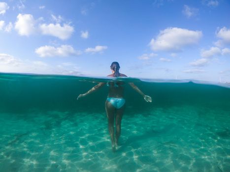 Woman walking into the sea, with her back turned. Formentera island, Spain. View at water level, photo with underwater dome.