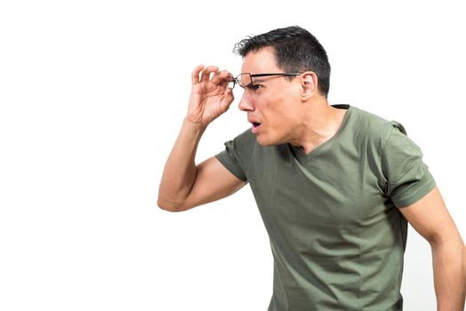Blind male in green t shirt lifting glasses and frowning while trying to see objects in distance against white background