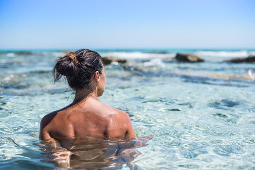 Woman bathing in a heavenly sea of turquoise water. With his back to the camera, looking at the horizon. Mid shot. Formentera island. Spain.