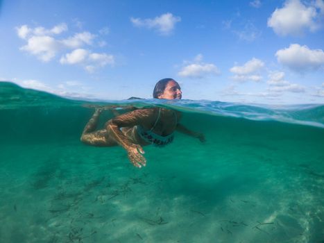 Woman swimming into the sea. View at water level, photo with underwater dome.