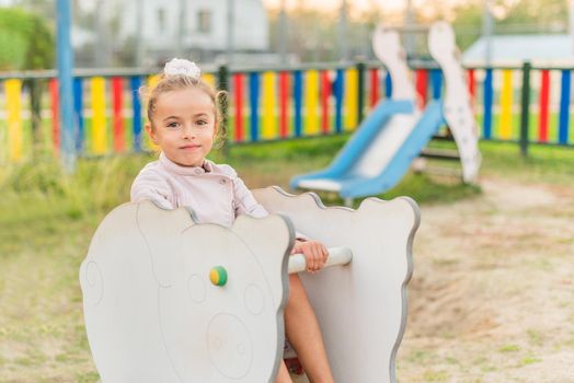 Portrait of a little girl sitting in a game of a playground looking at camera.