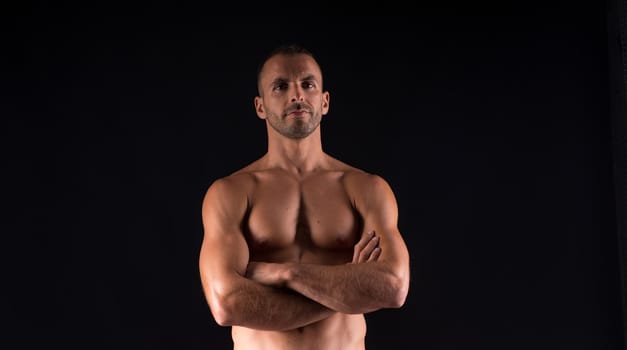 Athletic man without shirt. Mid shot. Black background.