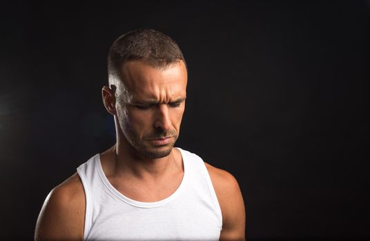 Sad athlete man in tank top. Close up. Black background.