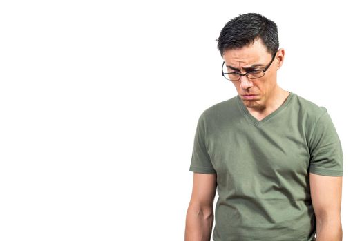 Sad man in green t shirt and glasses pouting lips and looking down while feeling depressed against white background