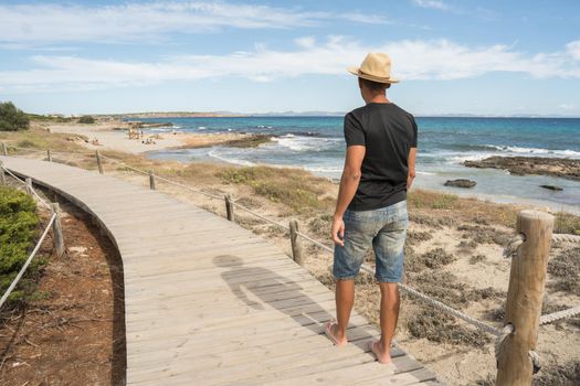 Man walking along a path of wooden boards by the sea. Long shot. Formentera island, Spain.