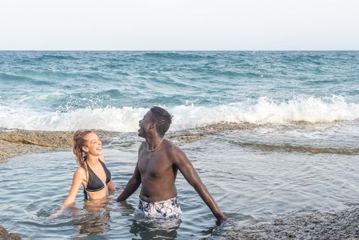 multiracial couple pouring water on each other in the sea, horizontal picture