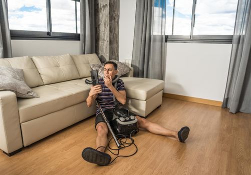 Man sitting on the floor in the living room trying to understand how a vacuum cleaner works. Full body.