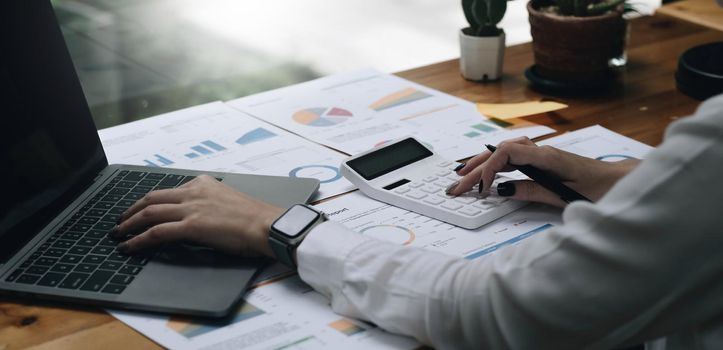 Close up Business woman using calculator and laptop for do math finance on wooden desk in office and business working background, tax, accounting, statistics and analytic research concept.