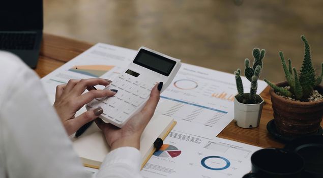 Close-up woman hand press calculator to calculate the company's financial results On the wooden table in the office and business work background, tax, accounting, statistics, and analytical research.