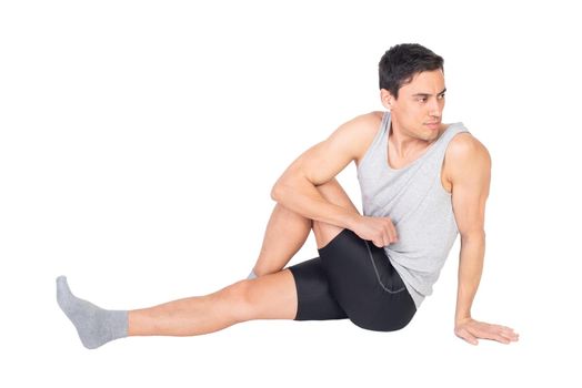 Full body of serious male in sportswear stretching buttocks muscles while sitting isolated on white background during training in studio