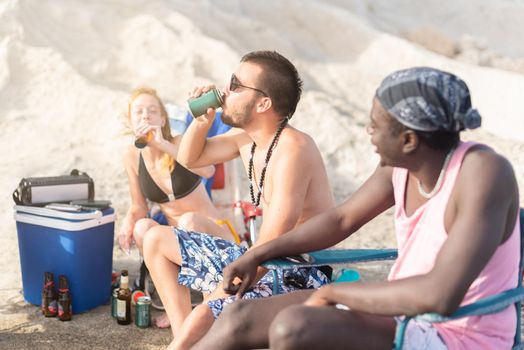 three people sitting on the beach doing picnic and drinking, close up view