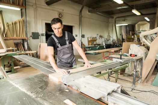 Worker cutting on a sliding table saw in a factory. Mid shot.