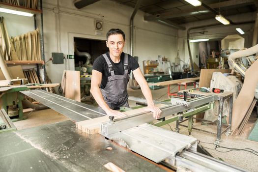 Worker cutting on a sliding table saw in a factory. Mid shot.