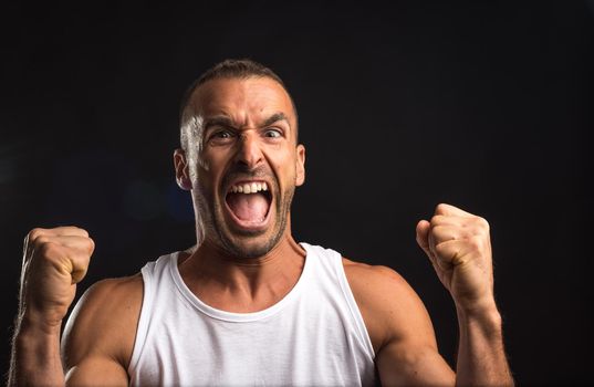 Athlete man in tank top celebrating a victory. Close up. Black background.