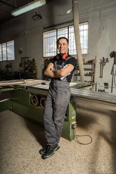 Worker standing with protective gear looking at camera smiling in a factory. Long shot, full body.