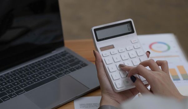 Close up Business woman using calculator and laptop for do math finance on wooden desk in office and business working background, tax, accounting, statistics and analytic research concept.