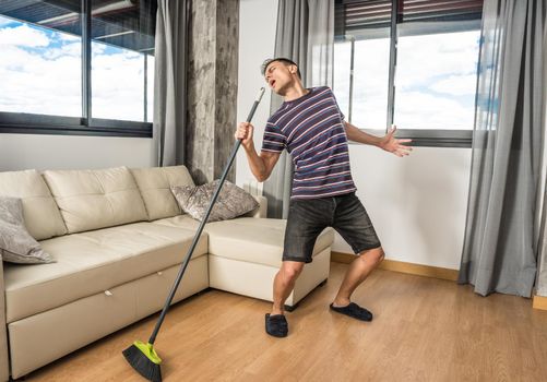 Man singing in the living room of his house holding the broom as if it were a microphone. Full body.