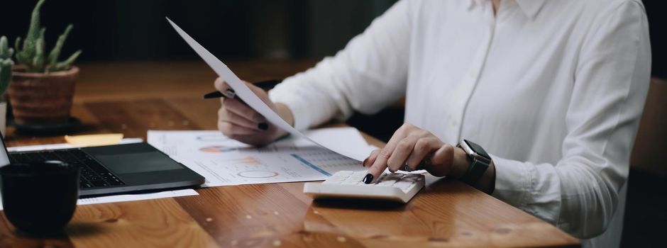 Close up Business woman using calculator and laptop for do math finance on wooden desk in office and business working background, tax, accounting, statistics and analytic research concept.