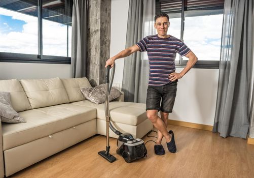 Smiling man in casual clothes vacuuming the living room. Full body.