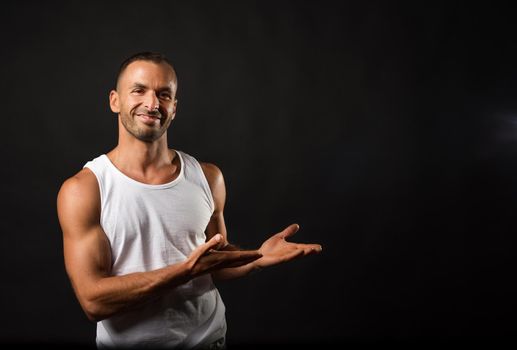 Smiling and athletic man in tank top pointing to copy space. Mid shot. Black background.