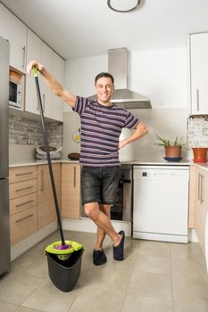 Smiling man wearing casual clothes and slippers mopping the kitchen floor. Full body.