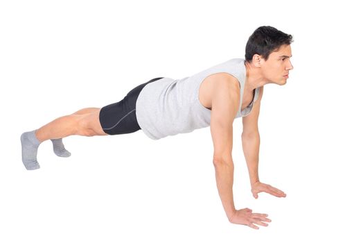 Full body side view of determined muscular male in sportswear doing push ups isolated on white background during intense workout